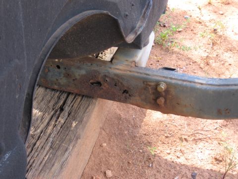 1980 Jeep CJ7 - Close-up view of a rusted vehicle frame rail and fender liner, supported by wooden blocks.