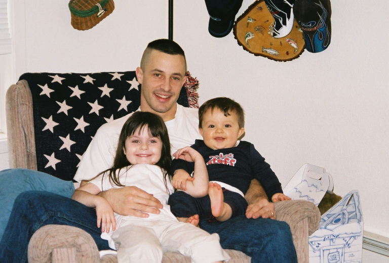 Man holding two young children while seated in an armchair indoors