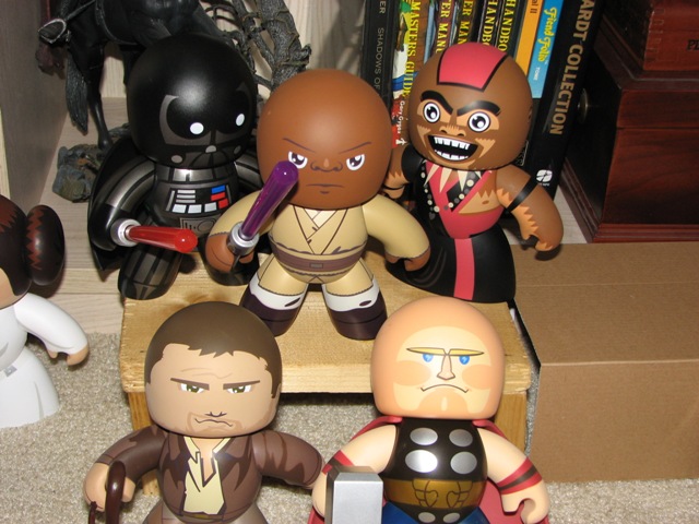 Collection of stylized Star Wars and Marvel character figures on a shelf with books