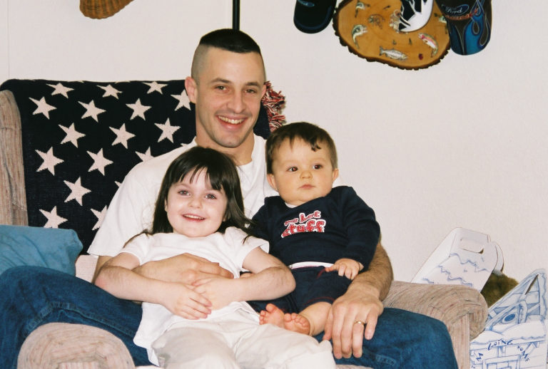 Man holding two young children in a chair indoors