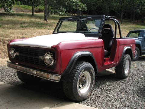 1968 Ford Bronco - 1968 Ford Bronco with a white hood and black roll cage is parked on gravel.