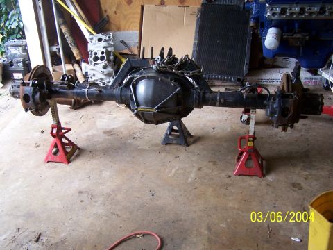 1979 Ford F-150 - A rear axle assembly is supported by jack stands in a garage, with engine parts visible.
