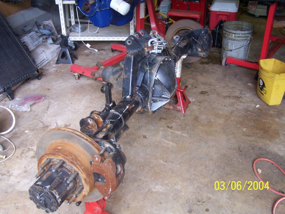 Front axle assembly with disc brakes, supported by jack stands in a garage