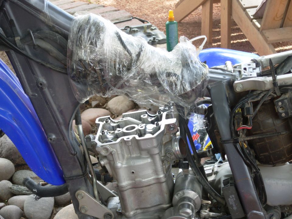 Motorcycle engine top exposed, intake covered in plastic wrap, blue bodywork