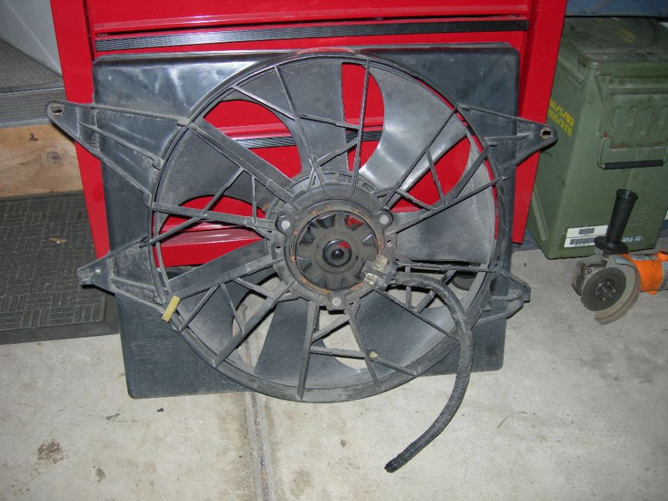 Radiator fan assembly with black plastic blades and a central motor housing, resting on a black plastic shroud