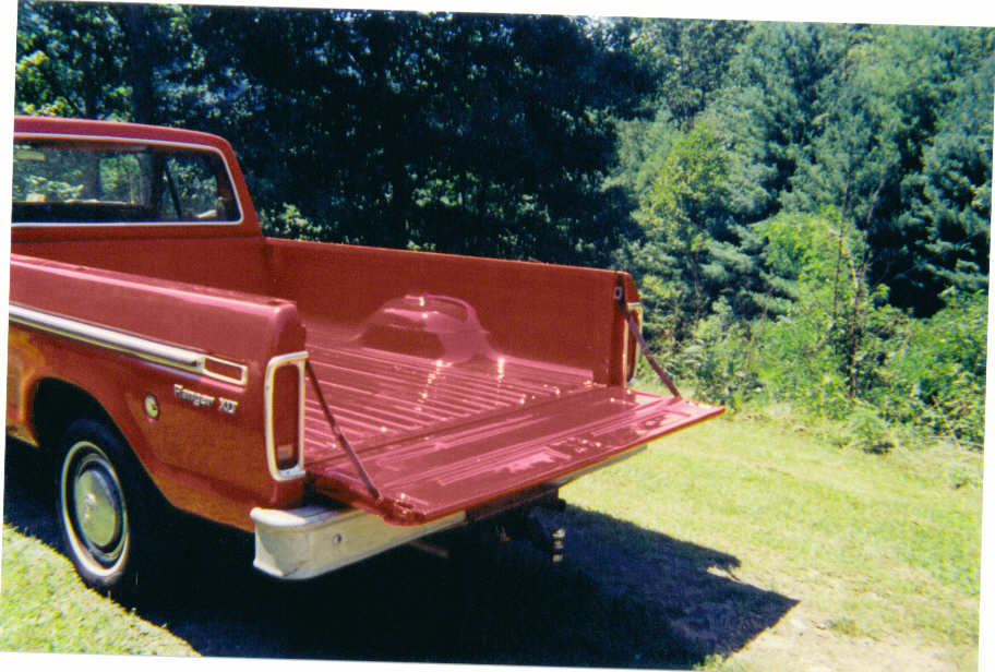 Red Ford pickup with tailgate down showing red bed floor, Ranger XLT badge, parked on grass