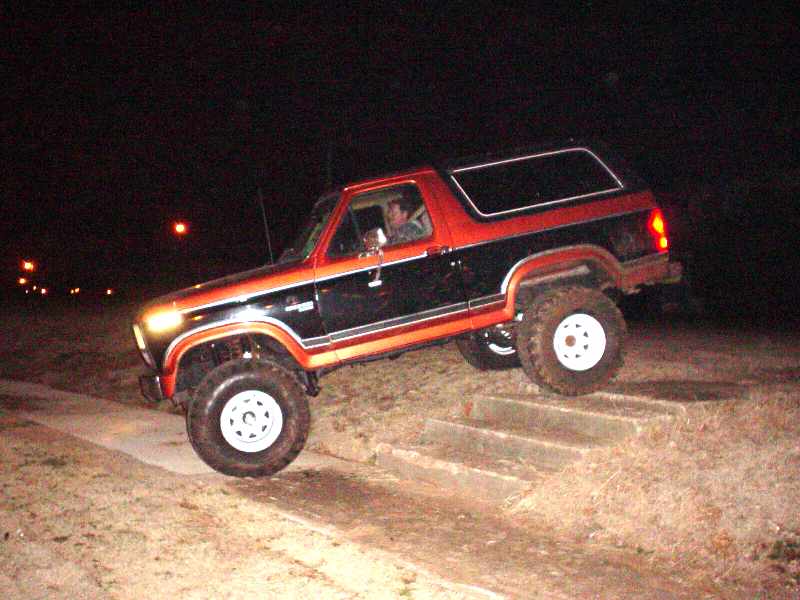 Black and orange 1984 Ford Bronco driving up stairs