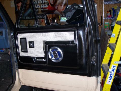1986 Ford Bronco - Close-up of a vehicle's interior door panel, a speaker and air vent, with a Star Wars poster reflected in the side mirror.