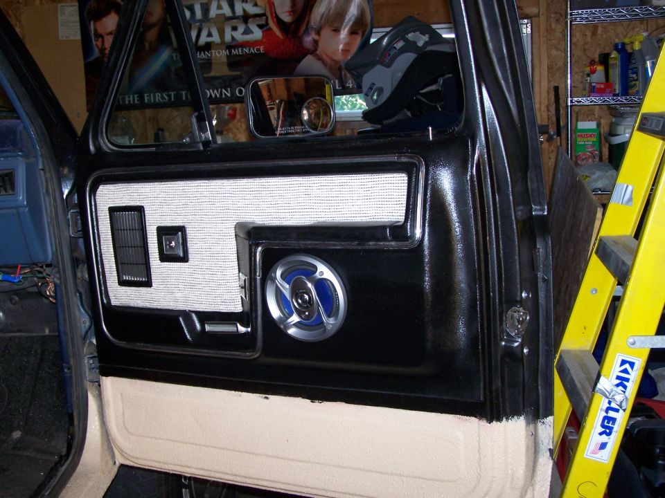 Interior of a vehicle door panel showing a speaker and vent. A Star Wars poster is visible in the window