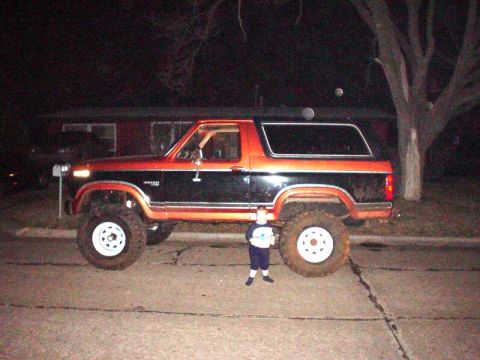 1984 Ford Bronco - A lifted Ford Bronco from the 1980s is shown parked at night with a child for scale.