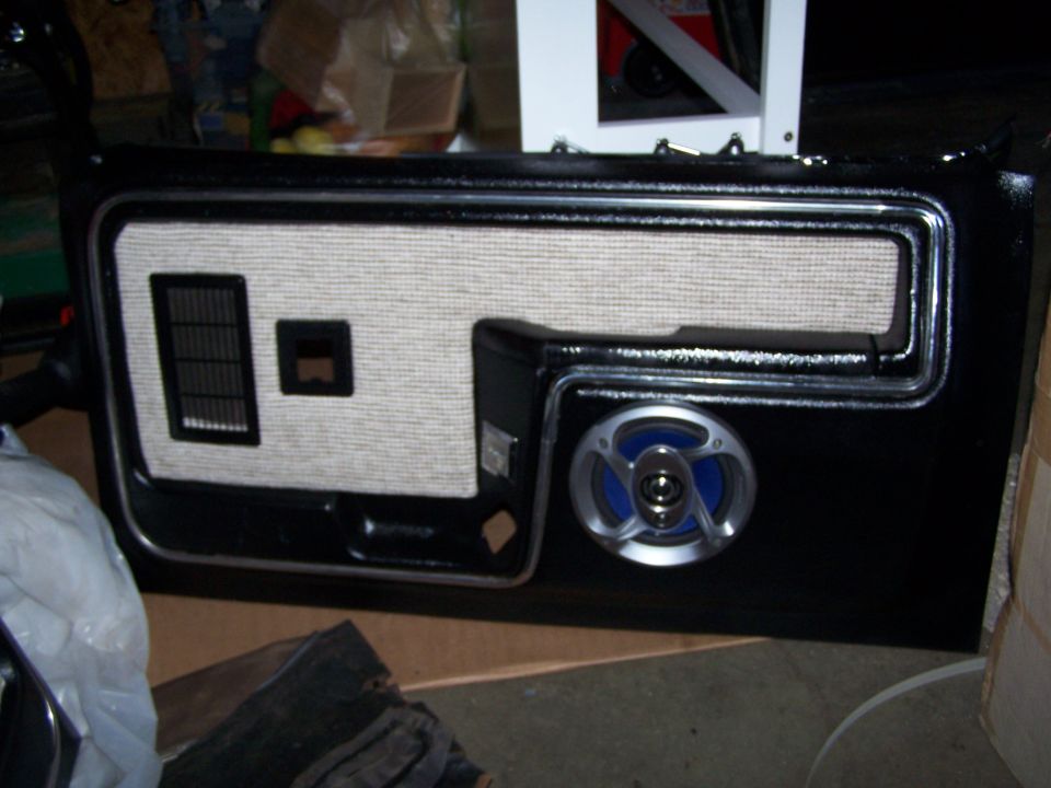 Black car door panel with textured fabric insert, speaker, and vent