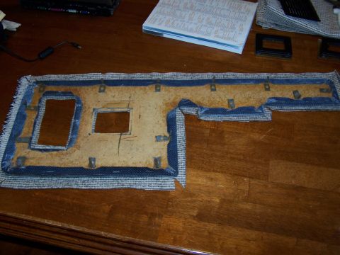 1986 Ford Bronco - A disassembled door panel insert with blue fabric trim and cutouts for mounting hardware is shown on a wooden surface.