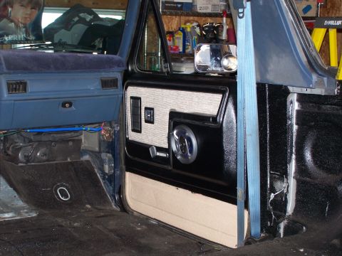 1986 Ford Bronco - Interior door panel and dashboard of a blue truck, showing door insert with speaker grille and window controls.