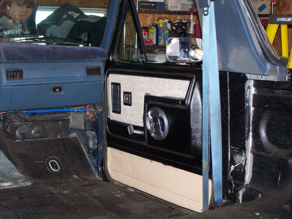 Interior door panel and dashboard of a blue truck, showing door insert with speaker grille and window controls