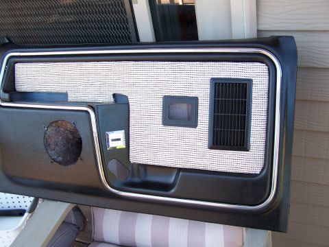 1986 Ford Bronco - A car door panel with a speaker opening and chrome trim is shown, resting on outdoor furniture.