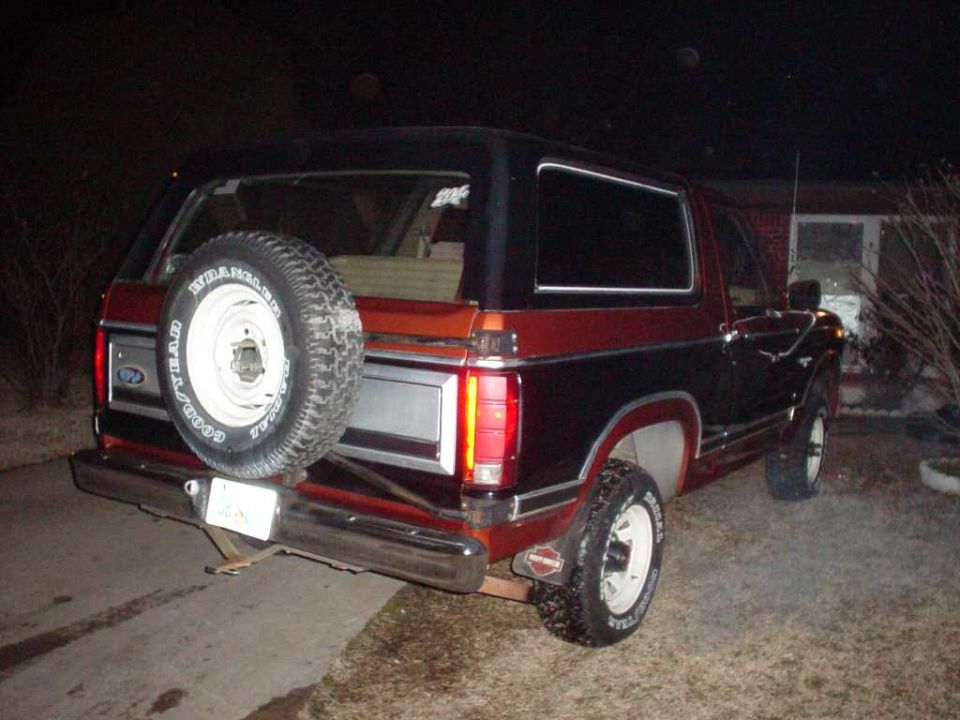 Rear view of a red and black Ford Bronco with a spare tire mounted on the back. The vehicle has a chrome bumper and a license plate