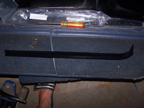 1986 Ford Bronco - A black door trim piece and a screwdriver are laid out on the blue carpeted interior of a vehicle.
