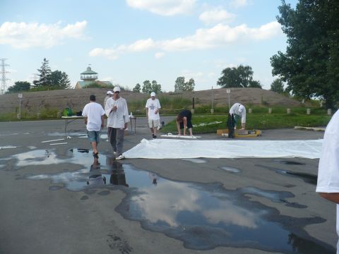 1993 Ford Probe - People are working outdoors on a cloudy day, setting up a large white sheet on a wet surface.