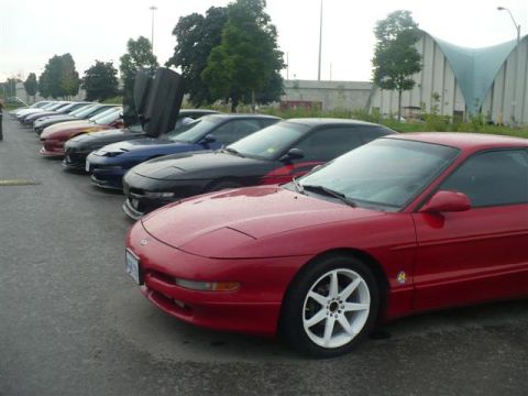 1993 Ford Probe - A line of Ford Probes are parked on asphalt, with a building and trees in the background.