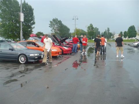 1993 Ford Probe - Several cars are parked in a lot with their hoods and doors open, while people stand around them.