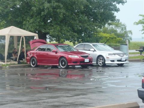 1993 Ford Probe - Two sedans are parked next to each other on a wet surface, with a tent and people in the background.