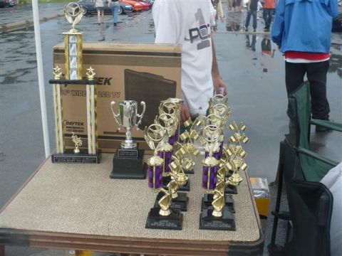 1993 Ford Probe - A collection of trophies are displayed on a table, with people and cars visible in the background.