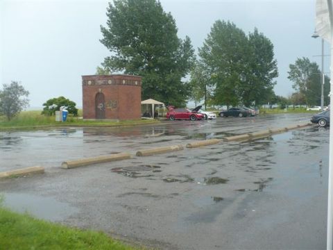 1993 Ford Probe - Several cars are parked in a wet lot near a brick building and trees.
