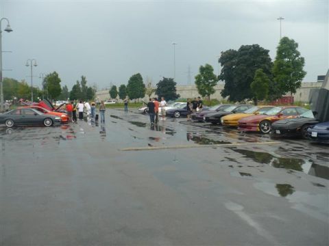 1993 Ford Probe - A gathering of cars and people in a wet parking lot under an overcast sky.