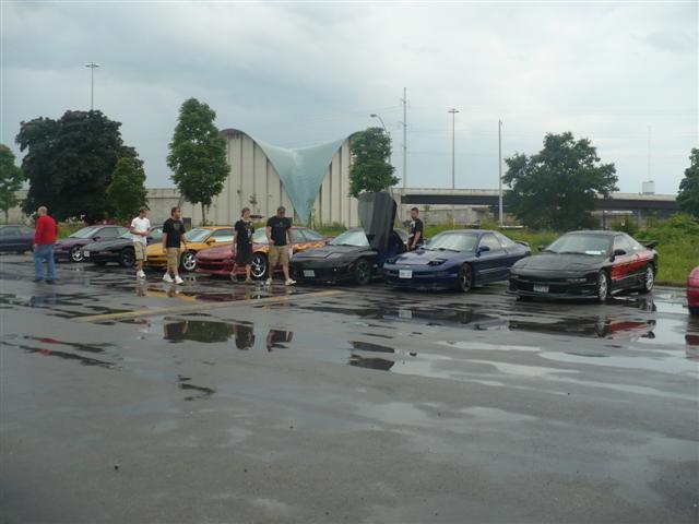 Several Ford Probes parked on a wet asphalt lot under a cloudy sky