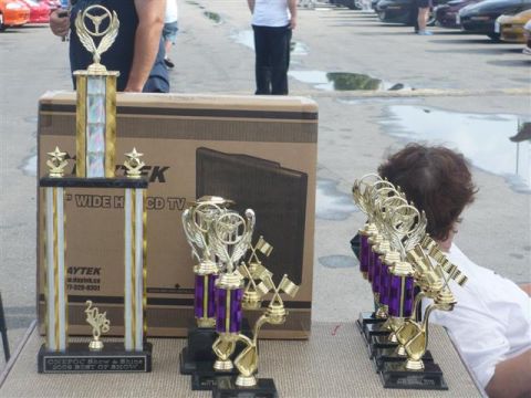 1993 Ford Probe - A collection of trophies sits on a table in front of a large box, with cars visible in the background.