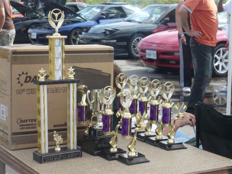 1993 Ford Probe - A collection of trophies sits on a table in front of several cars, suggesting a car show or competition.