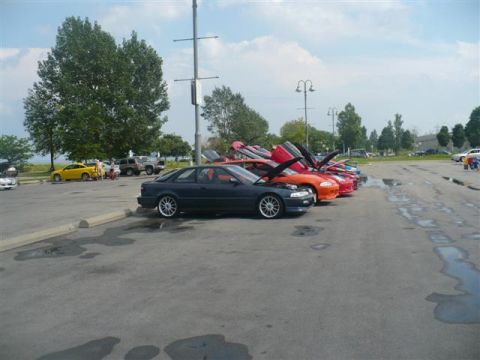1993 Ford Probe - A line of cars with hoods open are parked in a lot on a cloudy day.