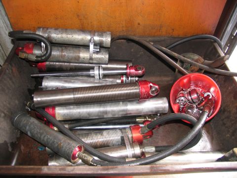 1984 Ford Bronco - A collection of silver and red shock absorbers with black hoses are piled inside a rusty metal container. A small red plastic cup filled wi…