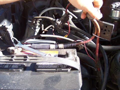 1996 Ford Bronco - Engine-bay view of a Motorcraft battery with a Stanley wrench resting on the terminal while a hand lifts a badly corroded red positive cabl…
