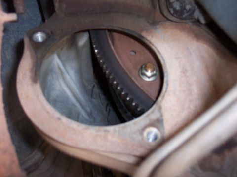 1996 Ford Bronco - A close-up view of the flywheel and starter ring gear through an opening in the transmission bell housing. A single bolt with a nut is visi…