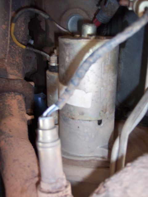 1996 Ford Bronco - Tight underhood/underbody shot of a starter motor body mounted alongside a rusty exhaust manifold and downpipe, with its terminal stud, cab…