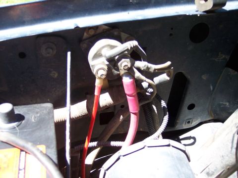 1996 Ford Bronco - Engine-bay close-up of a starter relay/solenoid mounted on the black inner fender, with heavy red and pink battery cables terminated at its…