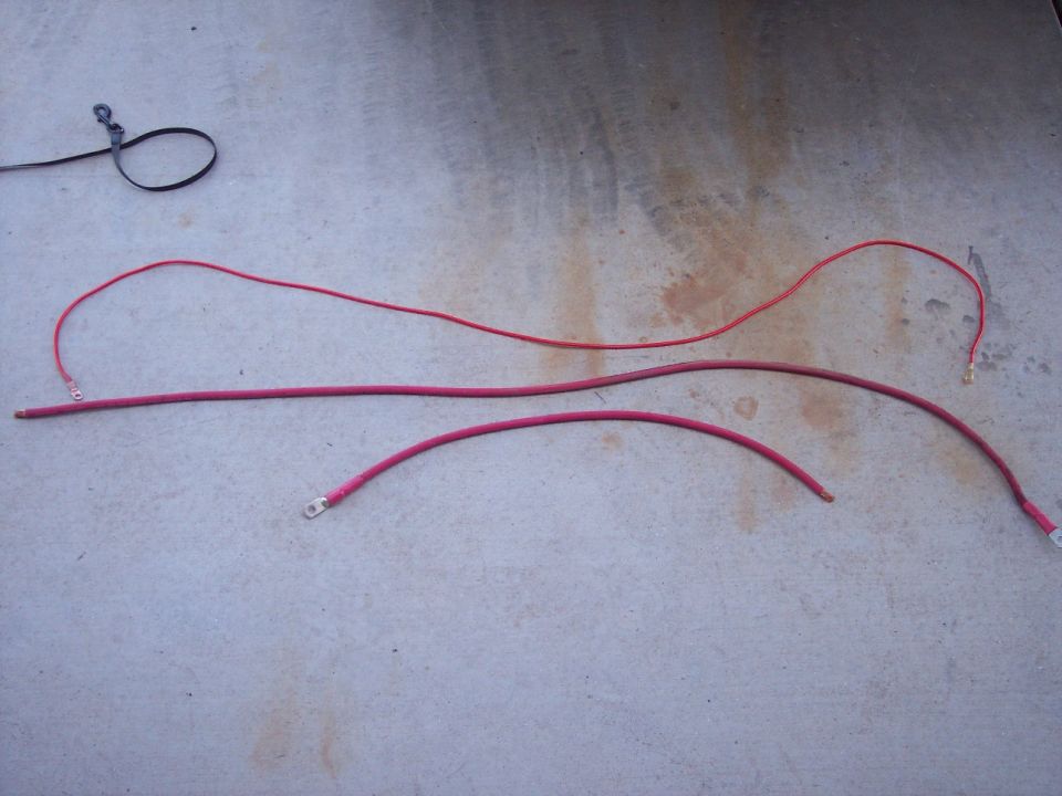 Three red automotive battery cables and a black leash on concrete.