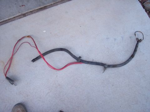 1996 Ford Bronco - A damaged red and black wire harness with a ribbed black protective sleeve is laid out on a concrete surface.