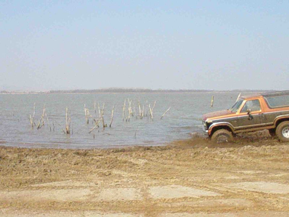 Orange and brown Ford Bronco driving into shallow water from a muddy bank