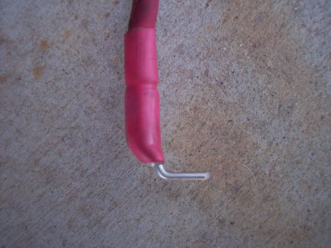1996 Ford Bronco - Close-up of the end of a heavy red battery cable lying on concrete, with red heat-shrink tubing sealing the insulation and a bare tinned co…