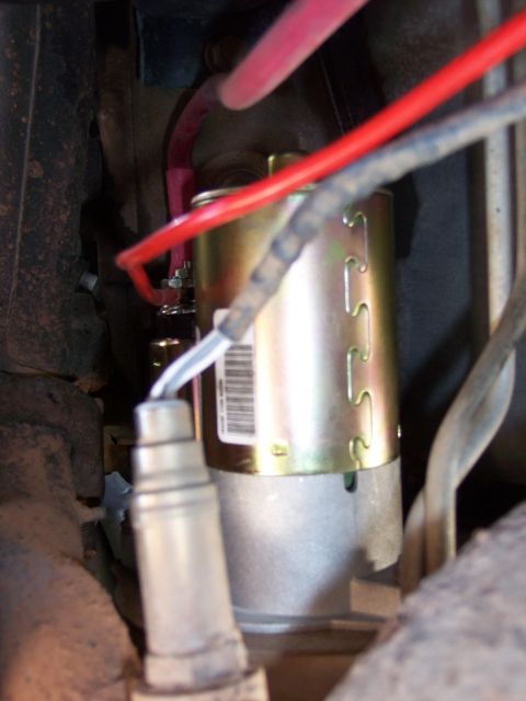 1996 Ford Bronco - A close-up view of a vehicle's starter motor with red and blue wires connected. A silver oxygen sensor is also visible in the foreground.