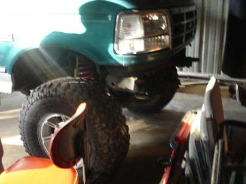 1996 Ford F-150 - A close-up, low-angle view of the front driver's side wheel and fender of a teal green Ford pickup truck. The large, knobby tire is promine…
