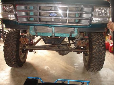 1996 Ford F-150 - A teal Ford F-150 pickup truck is shown from the front, focusing on the suspension and large off-road tires. The vehicle has a prominent gr…
