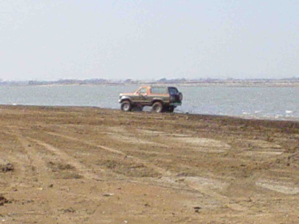 Tan SUV with spare tire on back, parked by water