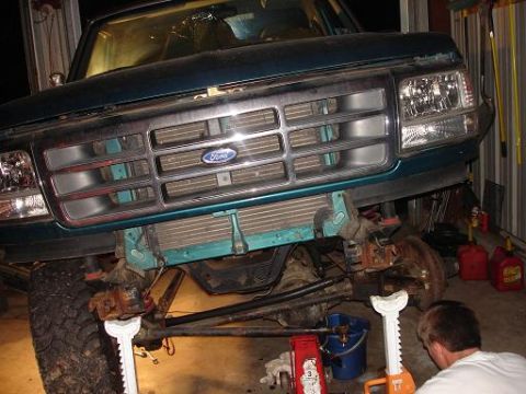 1996 Ford F-150 - The front end of a teal Ford F-150 pickup truck is lifted on jack stands in a garage. The grille, headlights, and front bumper are removed,…