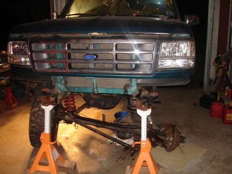 1996 Ford F-150 - The front end of a dark green pickup truck is elevated on jack stands in a garage setting. The front grille, headlights, and suspension com…