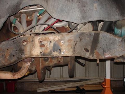1996 Ford F-150 - The underside of a vehicle, showing the rusty frame, exhaust pipes, and engine components. The vehicle is supported by jack stands.