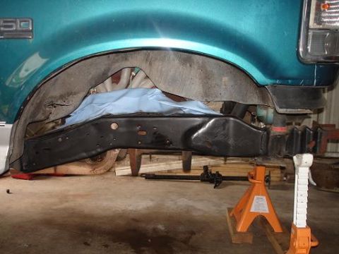 1996 Ford F-150 - The underside of a teal Ford F-150 pickup truck's wheel well area is shown, with the frame and suspension components visible. The vehicle i…