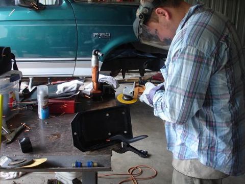 1996 Ford F-150 - A person wearing a face shield and plaid shirt is grinding metal near the side of a teal Ford F-150 pickup truck. Sparks are flying from th…